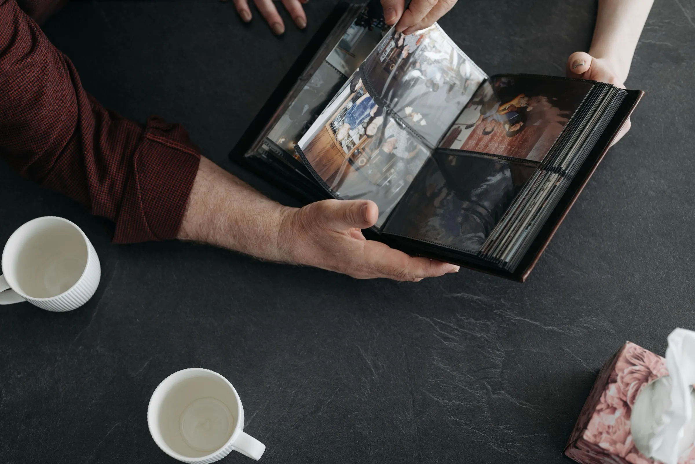 Hände halten einen Bilderrahmen, daneben zwei Kaffeetassen