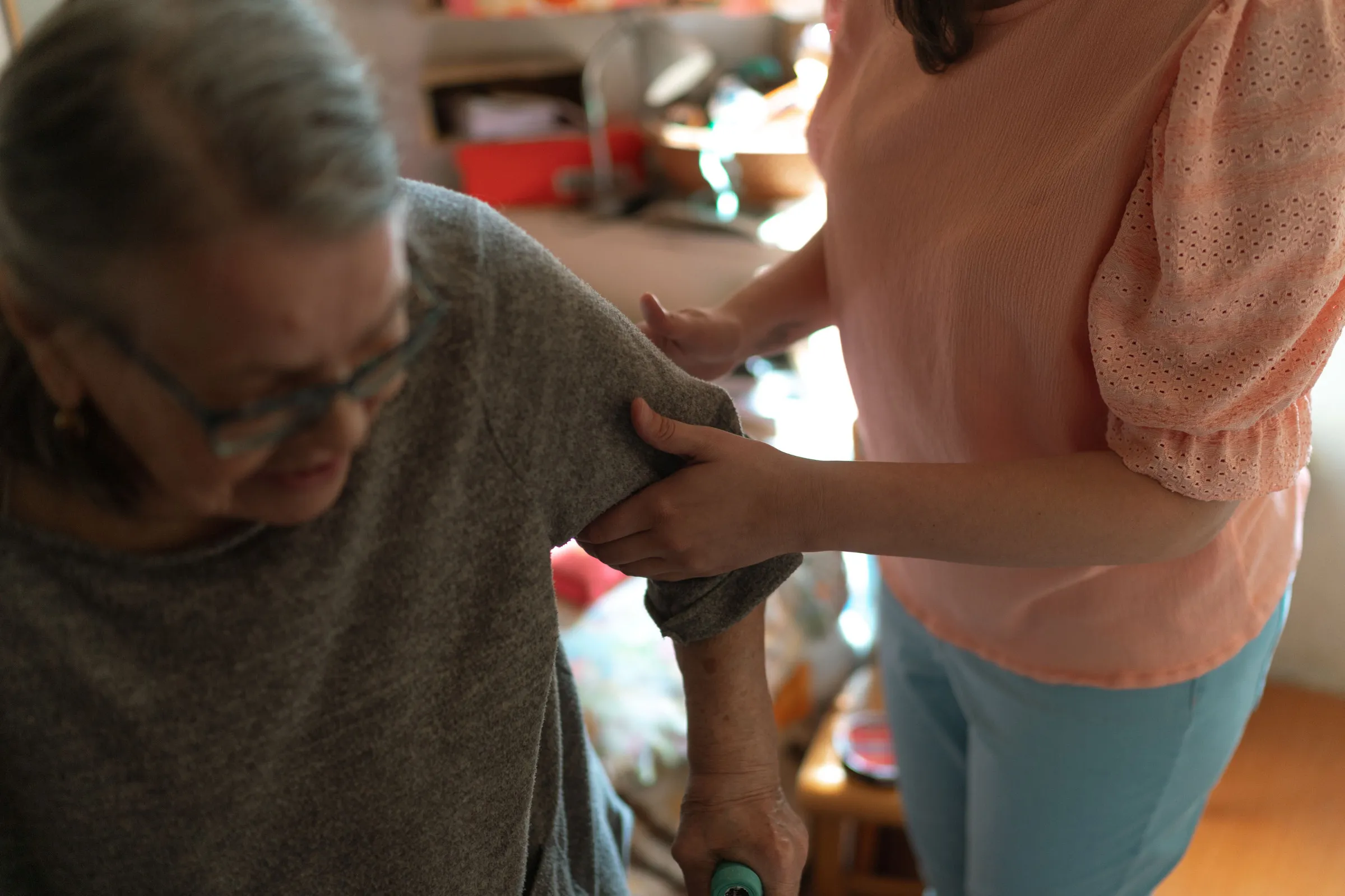 Pflegekraft stützt eine ältere Frau am Arm in ihrer Wohnung